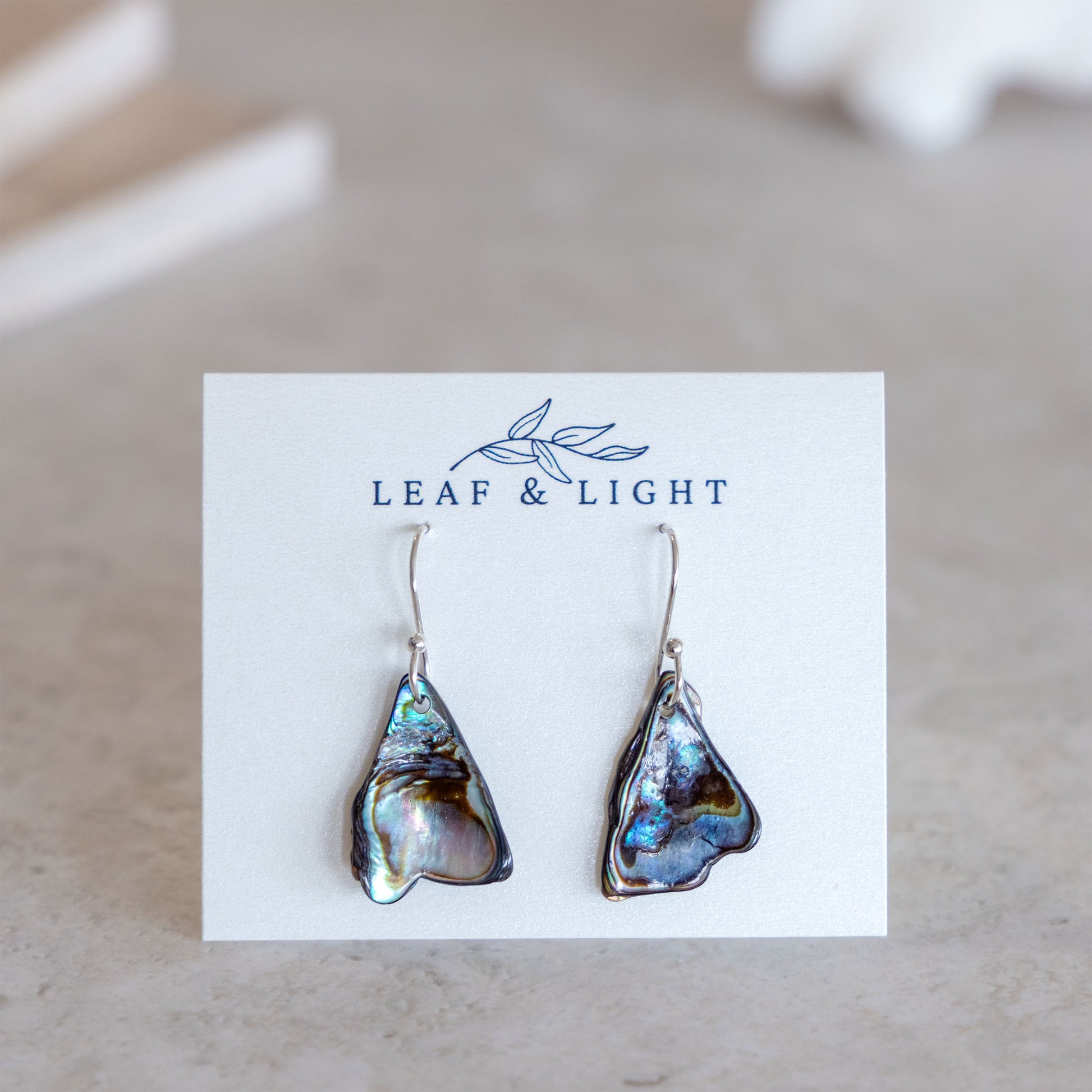 Pair of paua shell earrings on a 'Leaf & Light' branded card.
