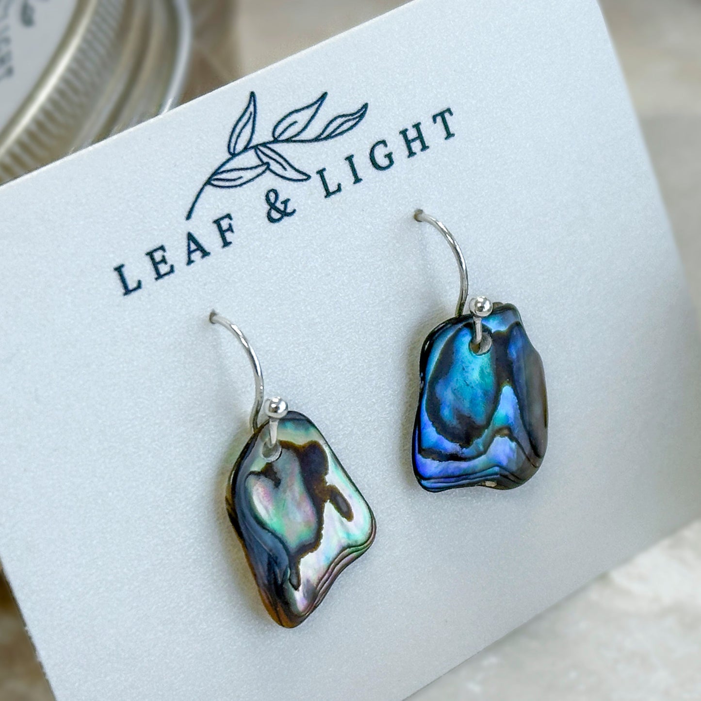 Pair of paua abalone shell earrings on a 'Leaf & Light' branded card.