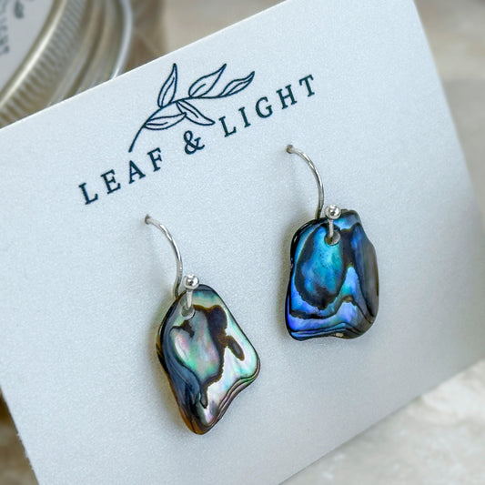Pair of paua abalone shell earrings on a 'Leaf & Light' branded card.